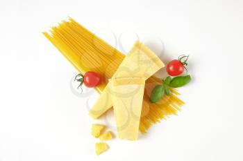 two wedges of fresh parmesan cheese, tomatoes and spaghetti on white background