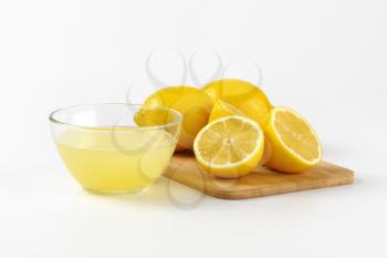 bowl of freshly squeezed lemon juice and ripe lemons on wooden cutting board