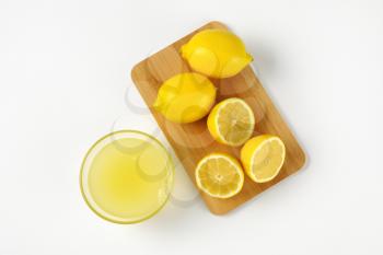 bowl of freshly squeezed lemon juice and ripe lemons on wooden cutting board