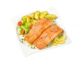 salmon fillets with roasted potatoes and vegetable garnish on square plate