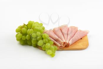 slices of ham and bunch of white grapes on wooden cutting board