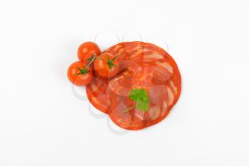 slices of chorizo salami and cherry tomatoes on white background