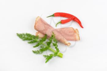slices of ham and red chili peppers on white background