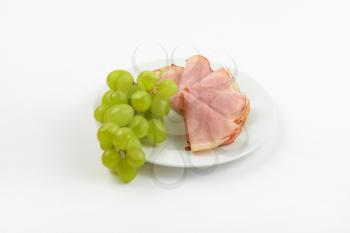 plate of ham slices with bunch of white grapes