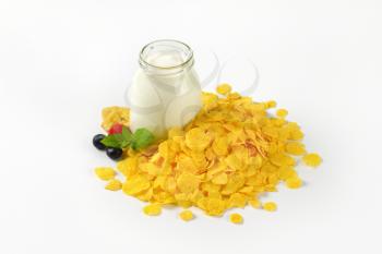 pile of corn flakes and glass of white yogurt on white background