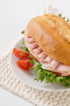 crusty roll sandwich with ham on white plate