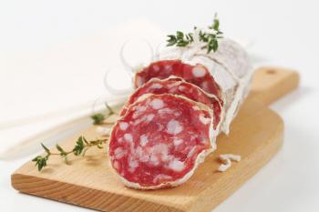 sliced dry cured sausage on wooden cutting board