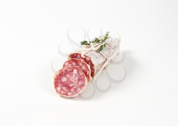 sliced dry cured sausage and thyme on white background