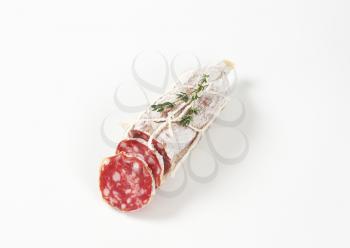 sliced dry cured sausage and thyme on white background
