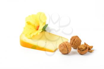 slice of gouda cheese with walnuts and hibiscus flower on white background