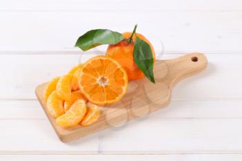 whole and sliced tangerines on wooden cutting board