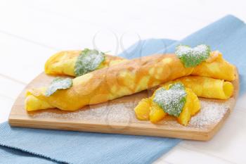 thin pancakes (crepes) with fresh orange slices on wooden cutting board