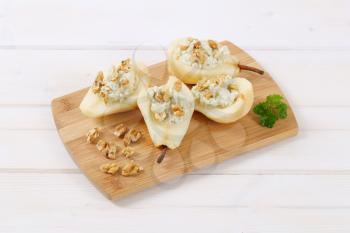 halved pears with blue cheese and walnuts on wooden cutting board