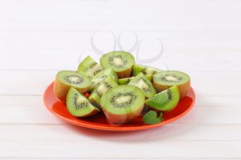 fresh kiwi fruits cut into halves and quarters on red plate