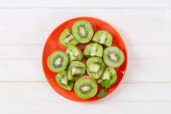 fresh kiwi fruits cut into halves and quarters on red plate