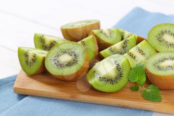 fresh kiwi fruits cut into halves and quarters on wooden cutting board