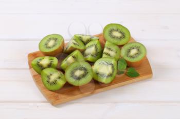 fresh kiwi fruits cut into halves and quarters on wooden cutting board