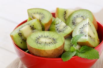 fresh kiwi fruits cut into halves and quarters in red bowl