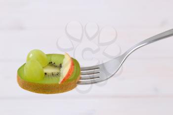 slice of kiwi with grapes and apple on fork