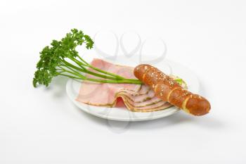 slices of asparagus coated ham with parsley and bread roll on white plate