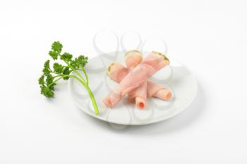 rolled slices of asparagus coated ham with parsley on white plate
