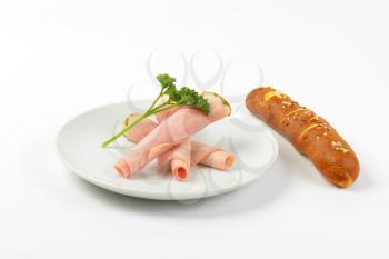 rolled slices of asparagus coated ham with parsley and bread roll on white plate