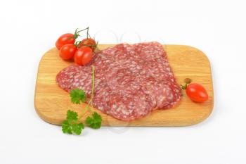 thin slices of salami and cherry tomatoes on wooden cutting board