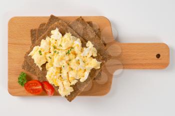 slices of fitness bread with scrambled eggs on wooden cutting board