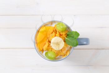 cup of corn flakes with milk and fresh fruit on white background