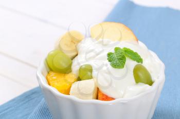 bowl of fresh fruit salad with white yogurt on blue place mat - close up