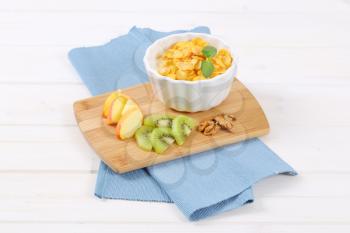 bowl of corn flakes with milk and fresh fruit on wooden cutting board
