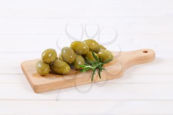 pile of green olives with fresh rosemary on wooden cutting board