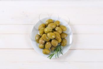 plate of green olives with fresh rosemary on white background