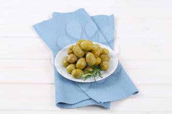 plate of green olives with fresh rosemary on blue place mat