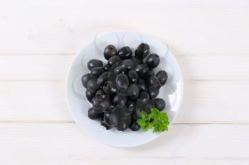 plate of black olives with fresh parsley on white background