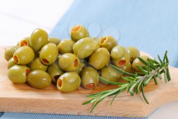 pile of green olives stuffed with red pepper on wooden cutting board - close up