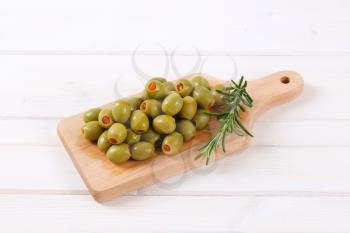 pile of green olives stuffed with red pepper on wooden cutting board