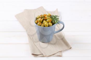 cup of green olives stuffed with red pepper on beige place mat