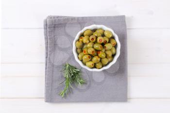 bowl of green olives stuffed with red pepper on grey place mat