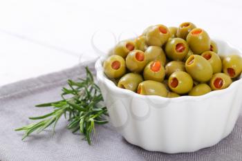 bowl of green olives stuffed with red pepper on grey place mat - close up