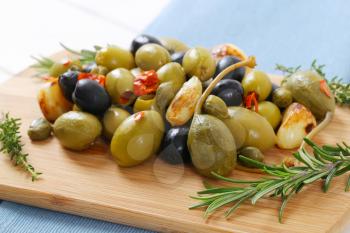 pile of pickled olives, capers, caper berries and garlic on wooden cutting board