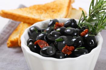 bowl of black olives with dried tomatoes and crispy toast on grey place mat - close up