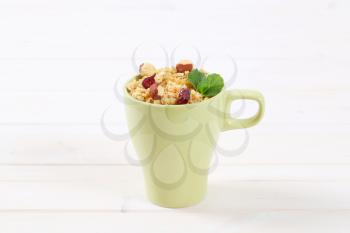 cup of granola with hazelnuts and dried cranberries on white wooden background