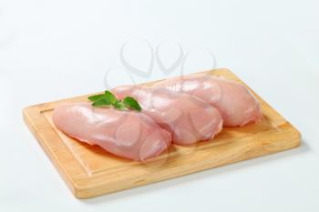Raw skinless chicken breast fillets on cutting board