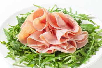 close up of fresh arugula leaves with sliced ham on white plate