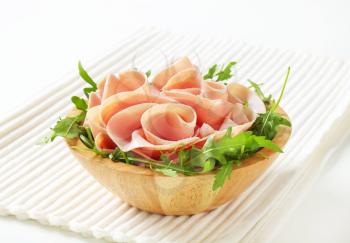 bowl of fresh arugula salad with sliced ham on white place mat