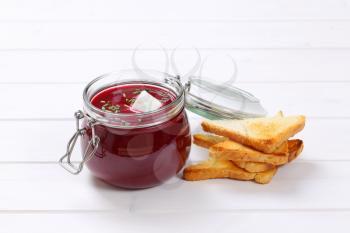 jar of beetroot cream soup with toast on white wooden background