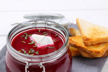 jar of beetroot cream soup with toast on grey place mat - close up