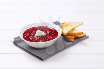 plate of beetroot cream soup with toast on grey place mat