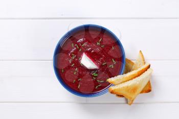 bowl of beetroot cream soup with toast on white wooden background